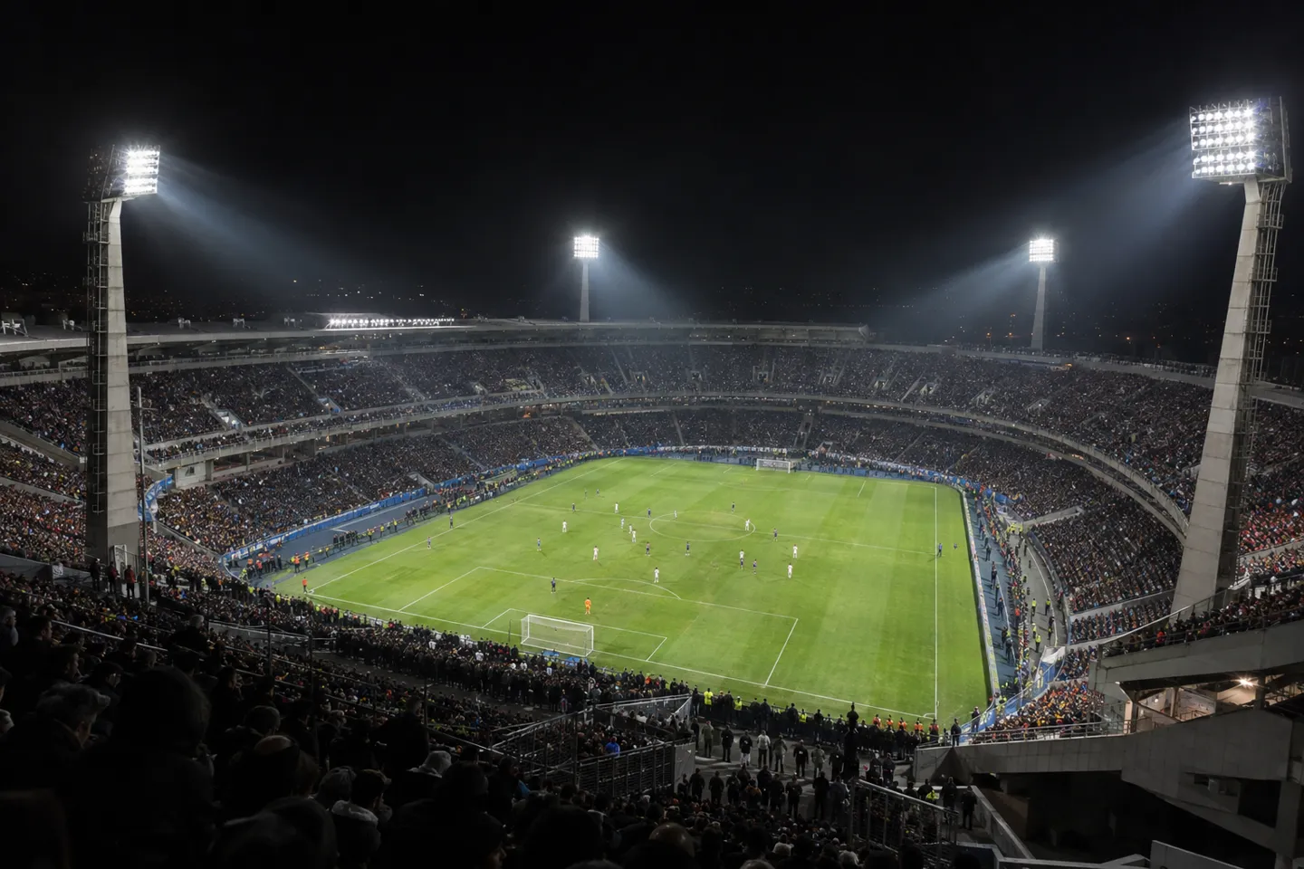 A professional football stadium glowing under four corner towers of LED floodlights at night — the broadcast-class end of the stadium lighting cost ladder.